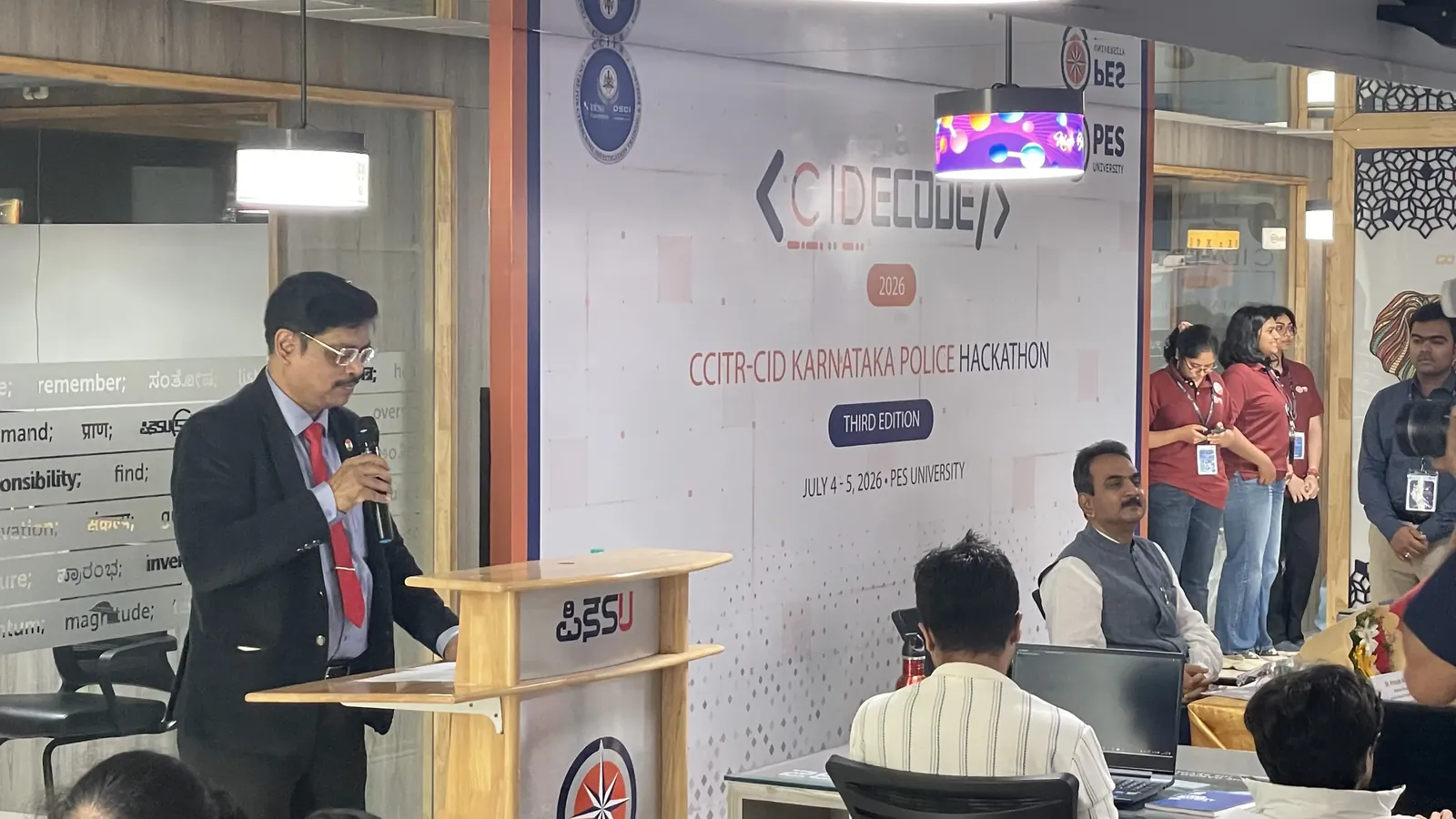 Teams at their desks with the CIDECODE 2026 banner and organizing volunteers in the background